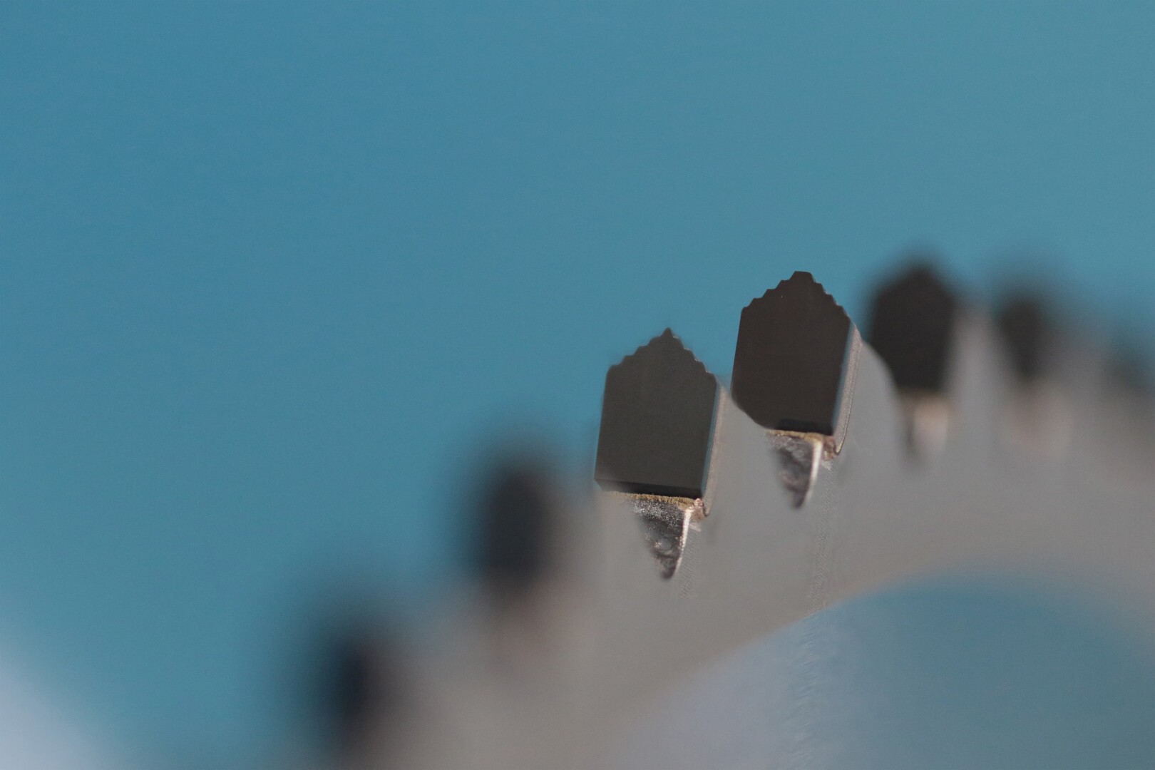 Gros plan des dents acérées et déchiquetées d’une lame de scie circulaire sur un fond bleu, avec une mise au point sélective mettant en évidence les bords métalliques de la lame.