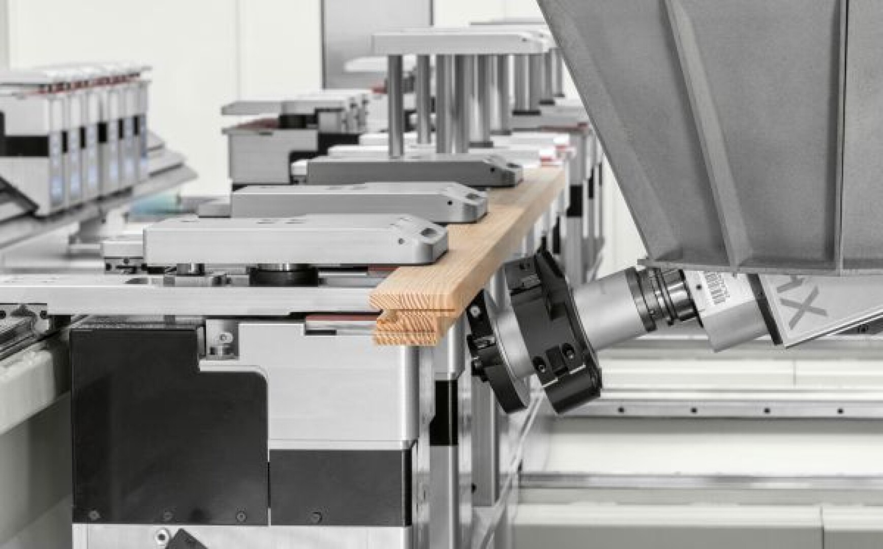 Un bras robotisé travaille avec un morceau de bois sur une chaîne de montage automatisée, entouré d'équipements métalliques de précision dans un environnement industriel moderne.